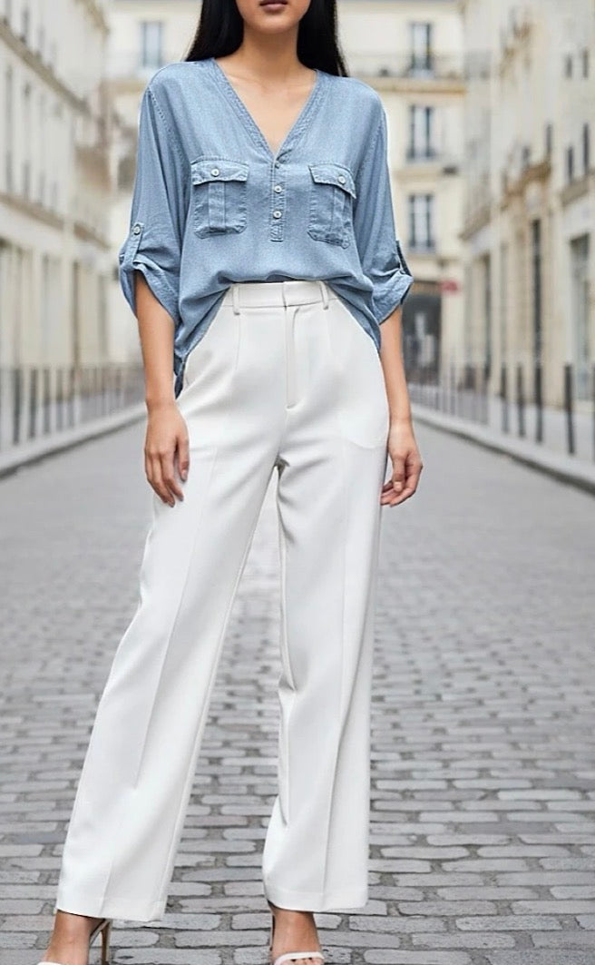 Person wearing a light blue denim shirt and white pants on a city street.