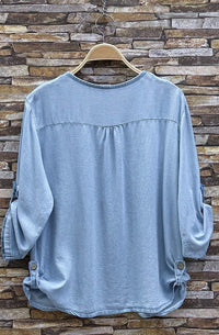 Light blue shirt on a wooden hanger against a stone wall background
