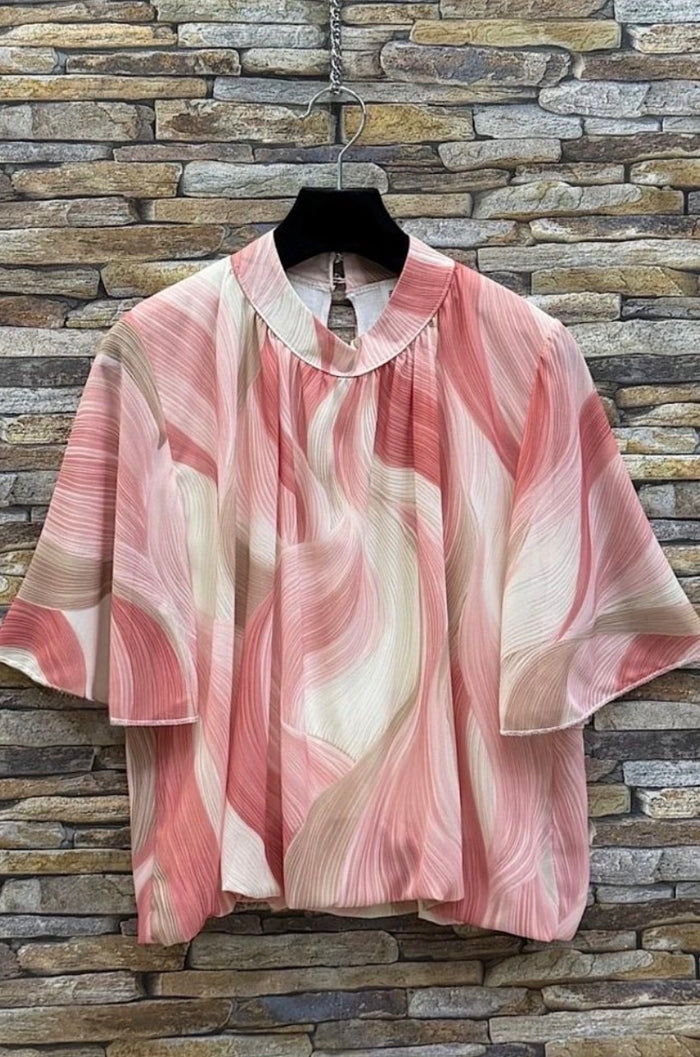 Pink and beige Agnes Print Blouse on a hanger against a stone wall background