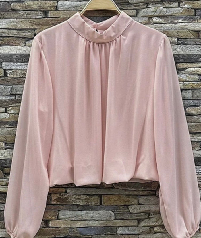 Anely Pink blouse with long sleeves on a hanger against a stone wall background