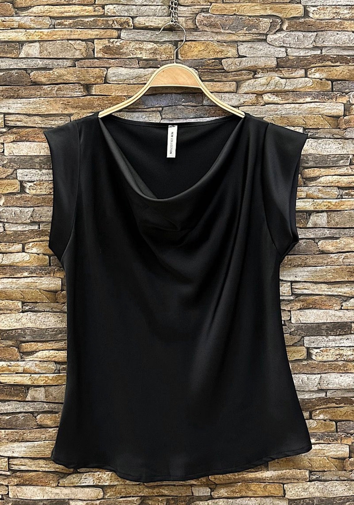 Black sleeveless top on a hanger against a stone wall background