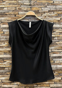 Black sleeveless top on a hanger against a stone wall background