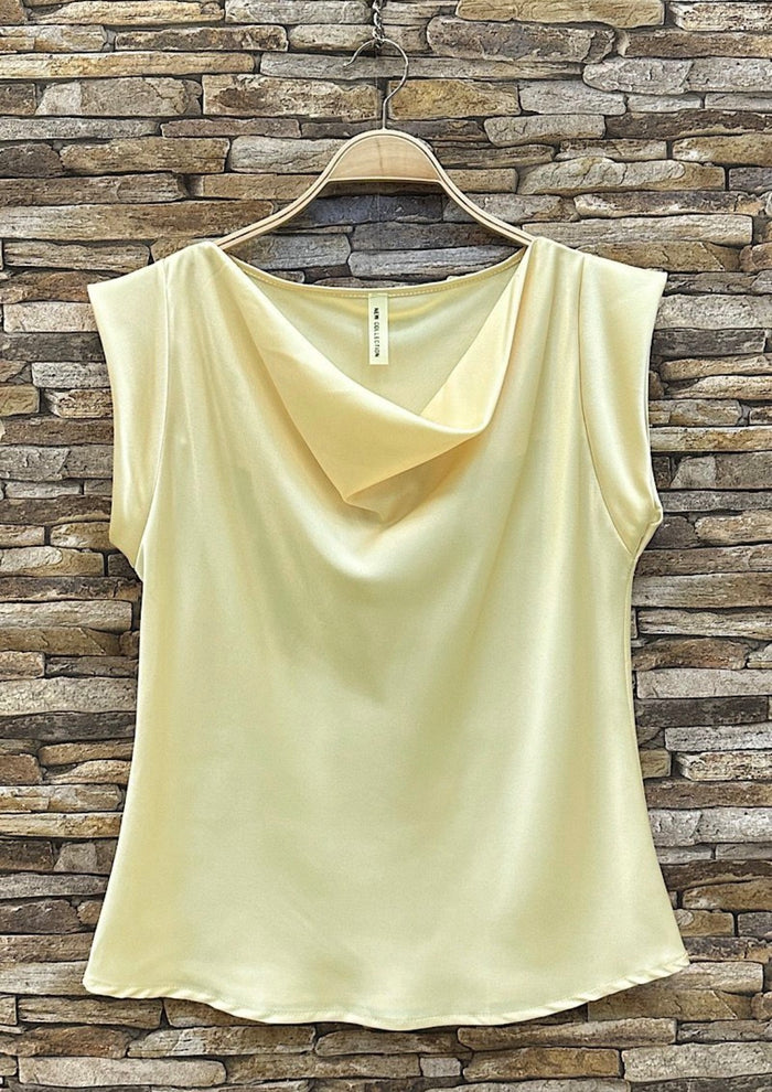 Light yellow sleeveless top on a hanger against a stone wall background