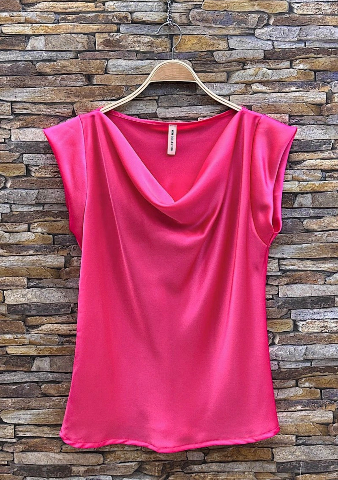 Pink sleeveless top on a hanger against a stone wall background