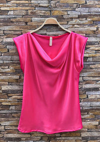 Pink sleeveless top on a hanger against a stone wall background