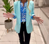 Person wearing a light blue Belle Print Top in a room with a plant and white wall.