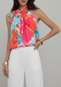 Woman wearing a colorful floral top and white pants on a plain background