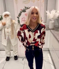 Woman in a Cindy Metallic V-Neck Print Top standing next to a person in a Santa Claus costume in a decorated room.