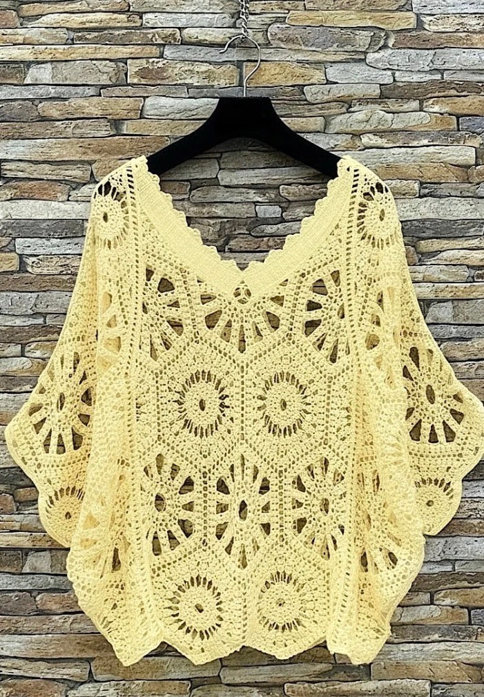 Yellow crochet shawl on a hanger against a stone wall background