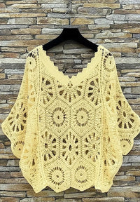 Yellow crochet shawl on a hanger against a stone wall background