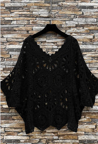 Black lace top on a hanger against a stone wall background