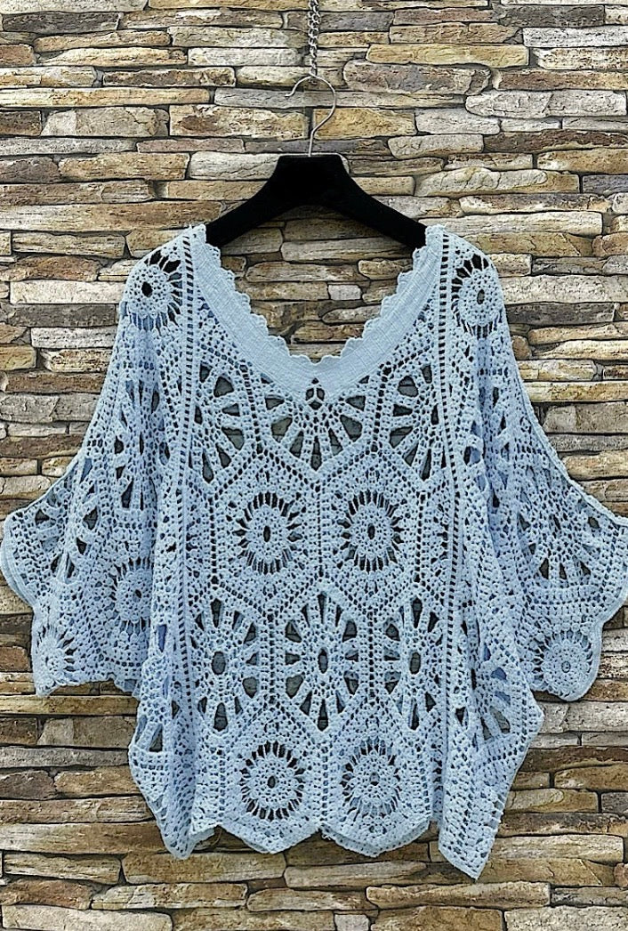Crocheted top on a hanger against a stone wall background
