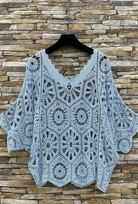 Crocheted top on a hanger against a stone wall background