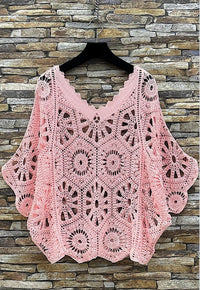 Pink crochet top on a hanger against a stone wall background