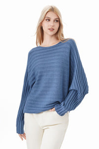 Woman wearing a blue sweater and white pants on a white background "Emily Batwing Top Blue colour"
