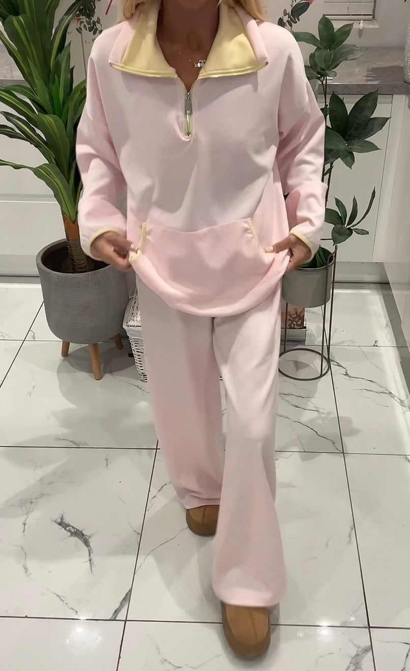 Person wearing a pink tracksuit in an indoor setting with plants and a tiled floor.