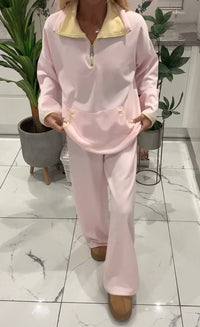 Person wearing a pink tracksuit in an indoor setting with plants and a tiled floor.