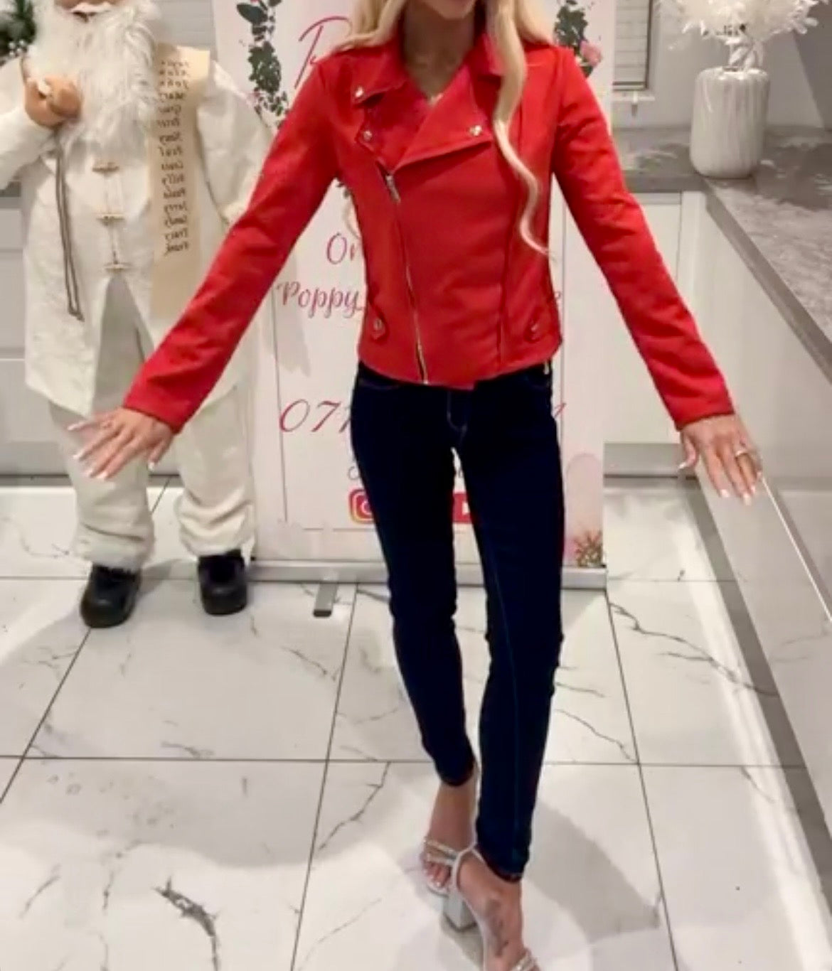 Person wearing a red Ivy Suede Detail Biker Jacket  and dark jeans standing in a store with a decorative background.