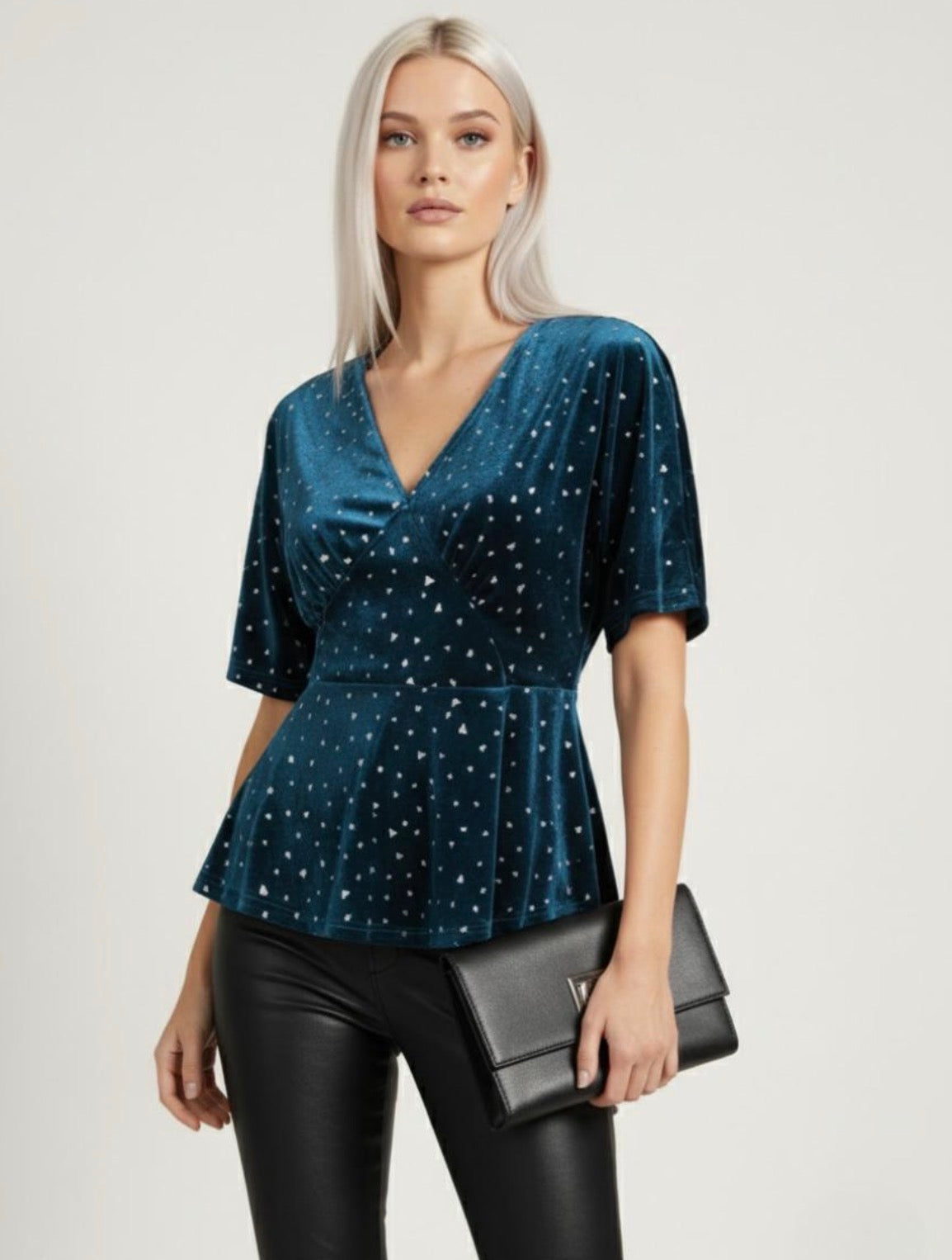 Woman wearing a blue peplum top with star patterns and black pants, holding a black clutch. Joyce Sparkle Detail V-Neck Top – Elegant Party Blouse