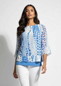 Woman wearing a blue and white patterned top with white pants on a plain background