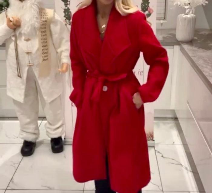 Person wearing a Kimmy red belted coat standing in a store with white furniture and decor.