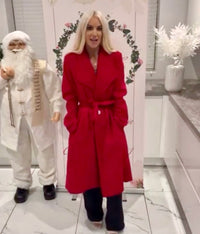 Person wearing a Kimmy red belted coat standing next to a decorative figure in a kitchen setting.