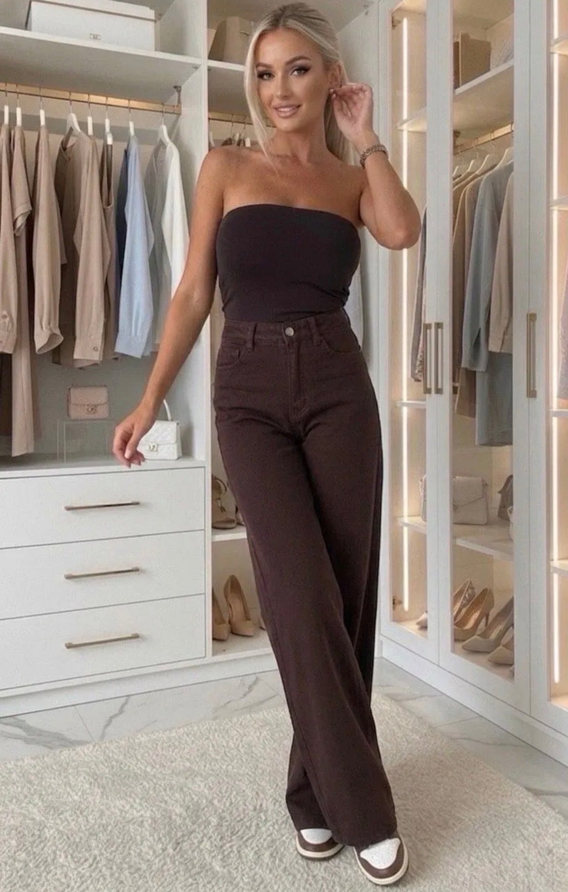 A woman modeling a dark brown strapless tube top and matching high-waisted wide-leg pants in a modern, well-lit walk-in closet.