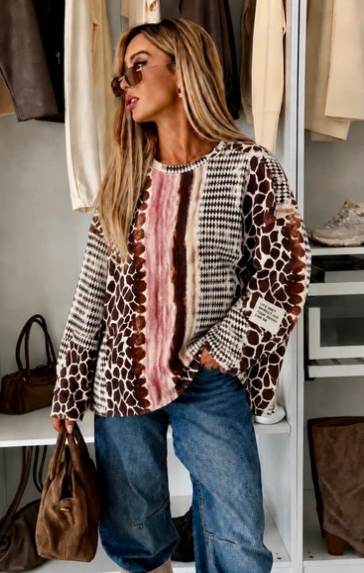 A woman wearing a long-sleeve knit top with mixed animal and stripe patterns in brown, beige, black, and pink, paired with blue jeans, standing in front of an open closet.