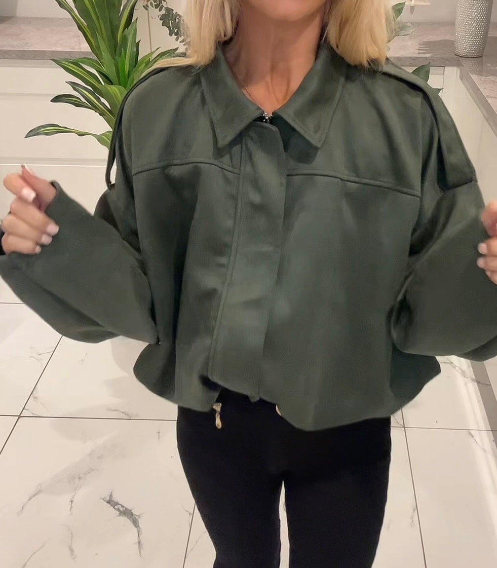 Person wearing a green jacket indoors with a plant in the background