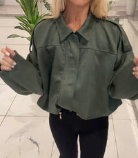 Person wearing a green jacket indoors with a plant in the background