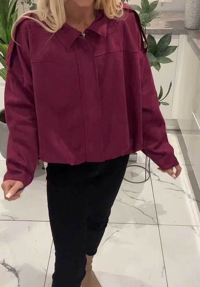 Person wearing a burgundy jacket and black pants indoors on a marble floor.