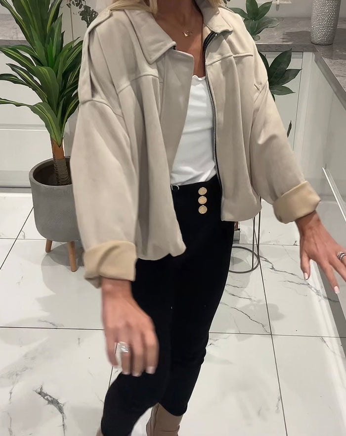 Person wearing a beige jacket over a white shirt and black pants in a kitchen.