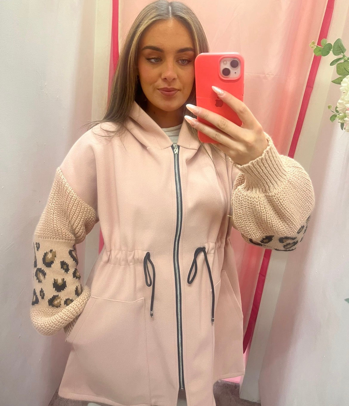 Woman taking a mirror selfie wearing a light pink jacket with leopard print sleeves.