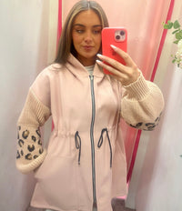 Woman taking a mirror selfie wearing a light pink jacket with leopard print sleeves.