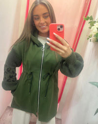 Woman taking a mirror selfie wearing a green jacket with a pink background