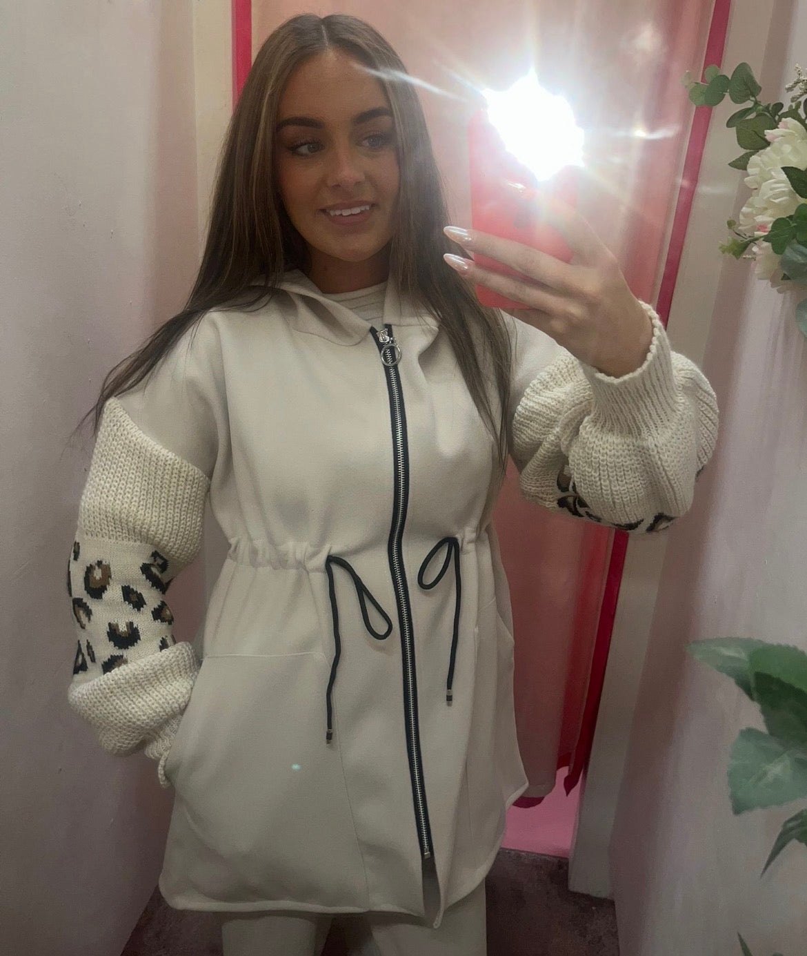 Woman taking a mirror selfie wearing a light-colored jacket with leopard print sleeves.