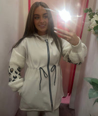 Woman taking a mirror selfie wearing a light-colored jacket with leopard print sleeves.