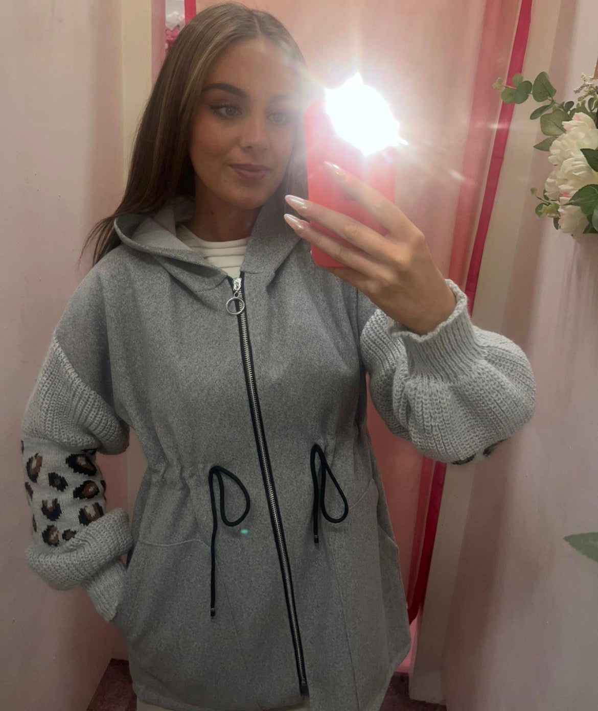 Person wearing a gray zip-up hoodie with leopard print sleeves, taking a mirror selfie.