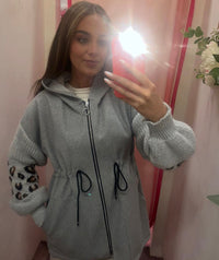Person wearing a gray zip-up hoodie with leopard print sleeves, taking a mirror selfie.