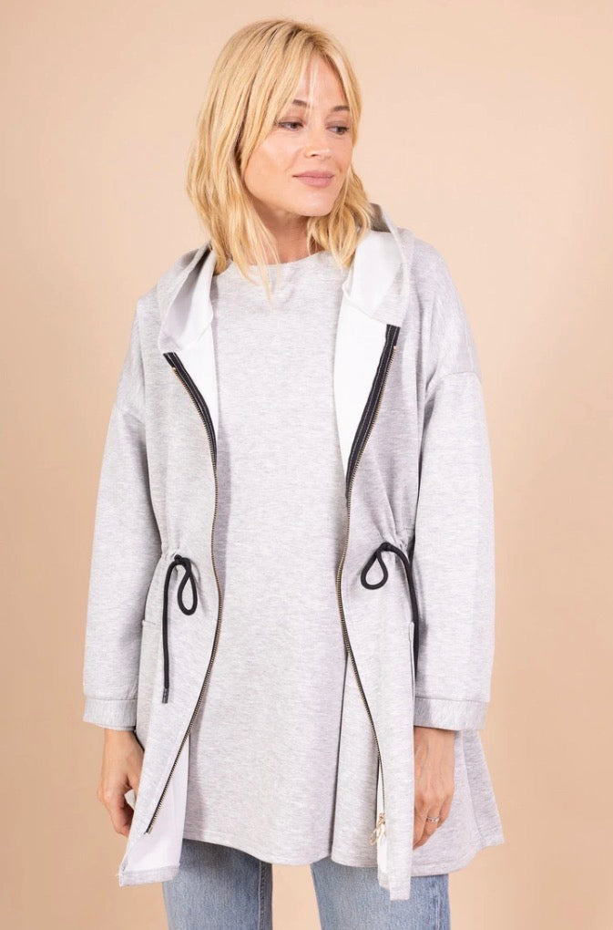 Woman wearing a gray hooded coat with black zippers on a beige background