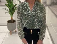 Person wearing a Lucinda Print Band Top Khaki setting with a plant and tiled floor.