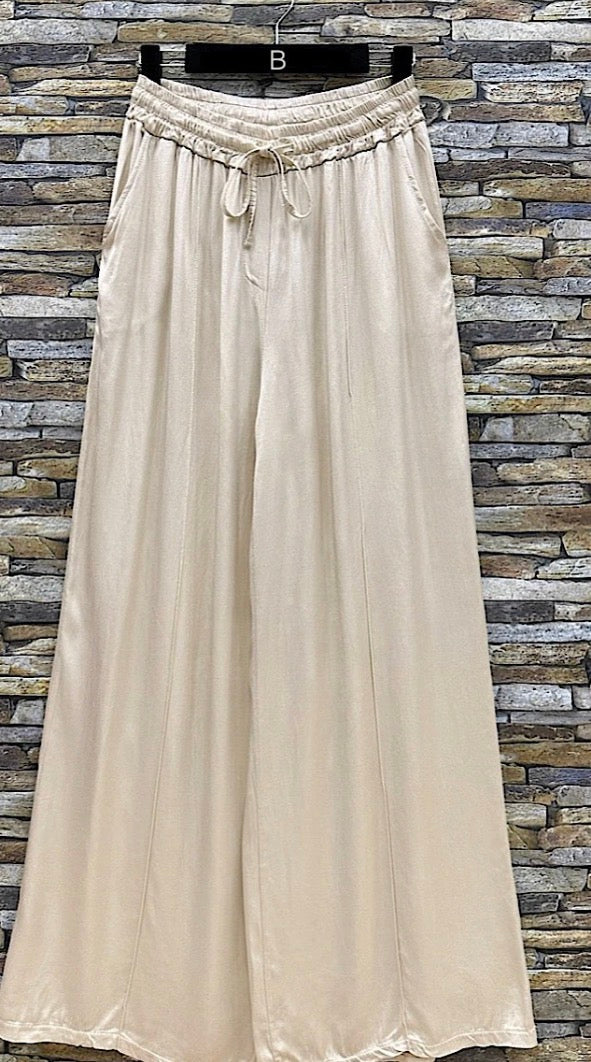 Beige wide-leg pants with a drawstring waist on a stone wall  Lucy Satin Wide Leg Pants for Modern Women background