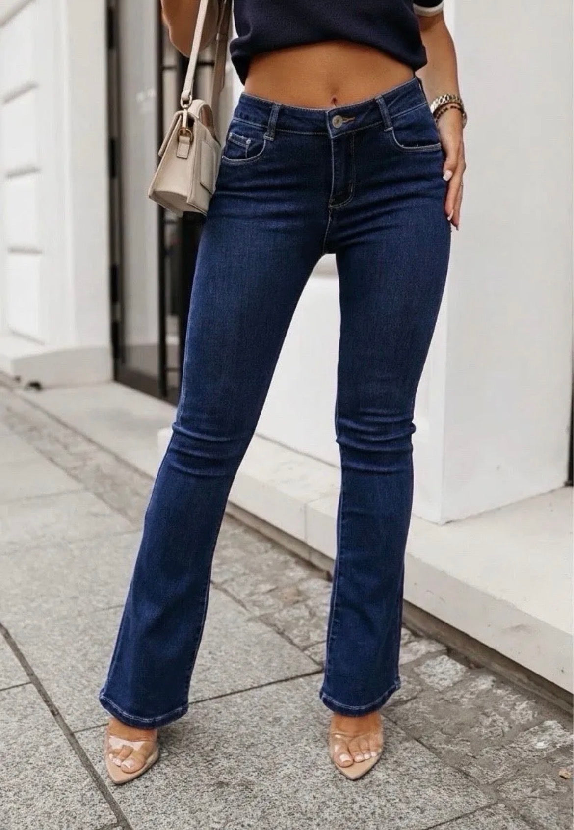 Person wearing blue jeans standing on a sidewalk with a white building in the background