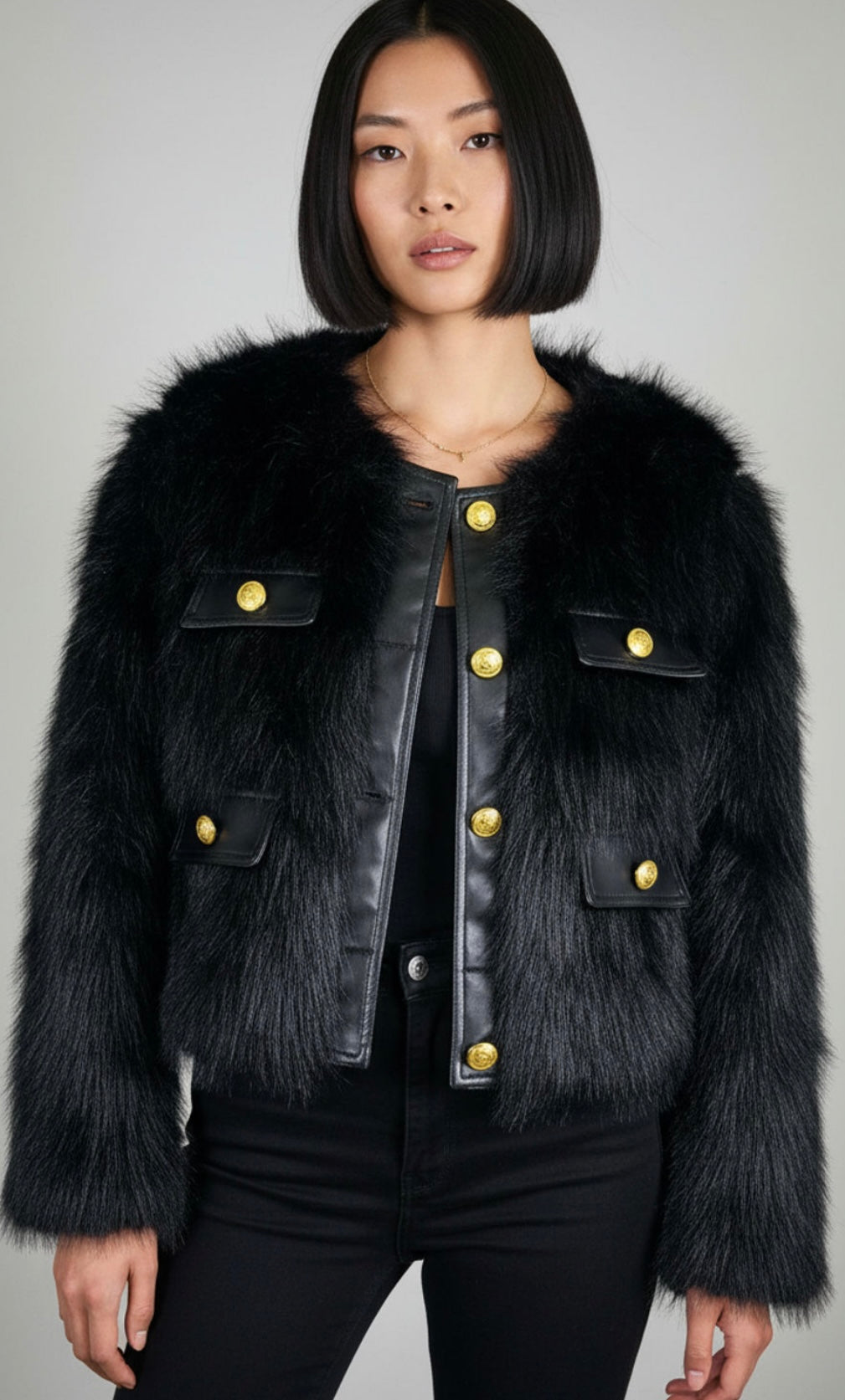 Woman wearing a black fur-trimmed jacket with gold buttons on a gray background