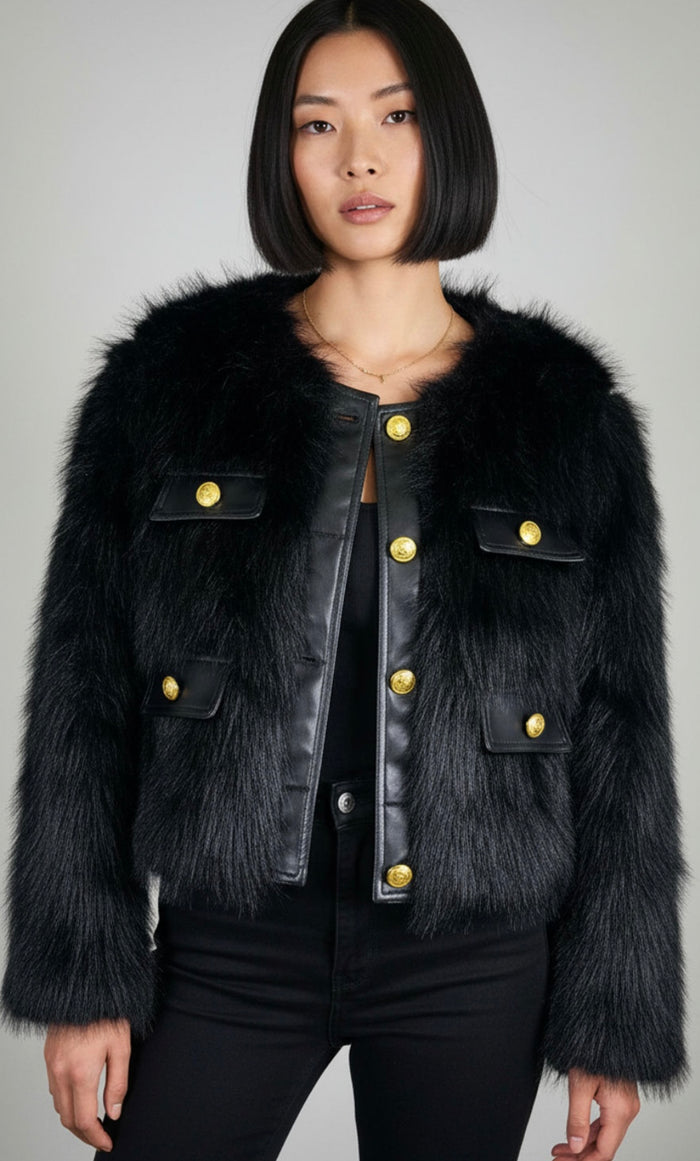 Woman wearing a black fur-trimmed jacket with gold buttons on a gray background