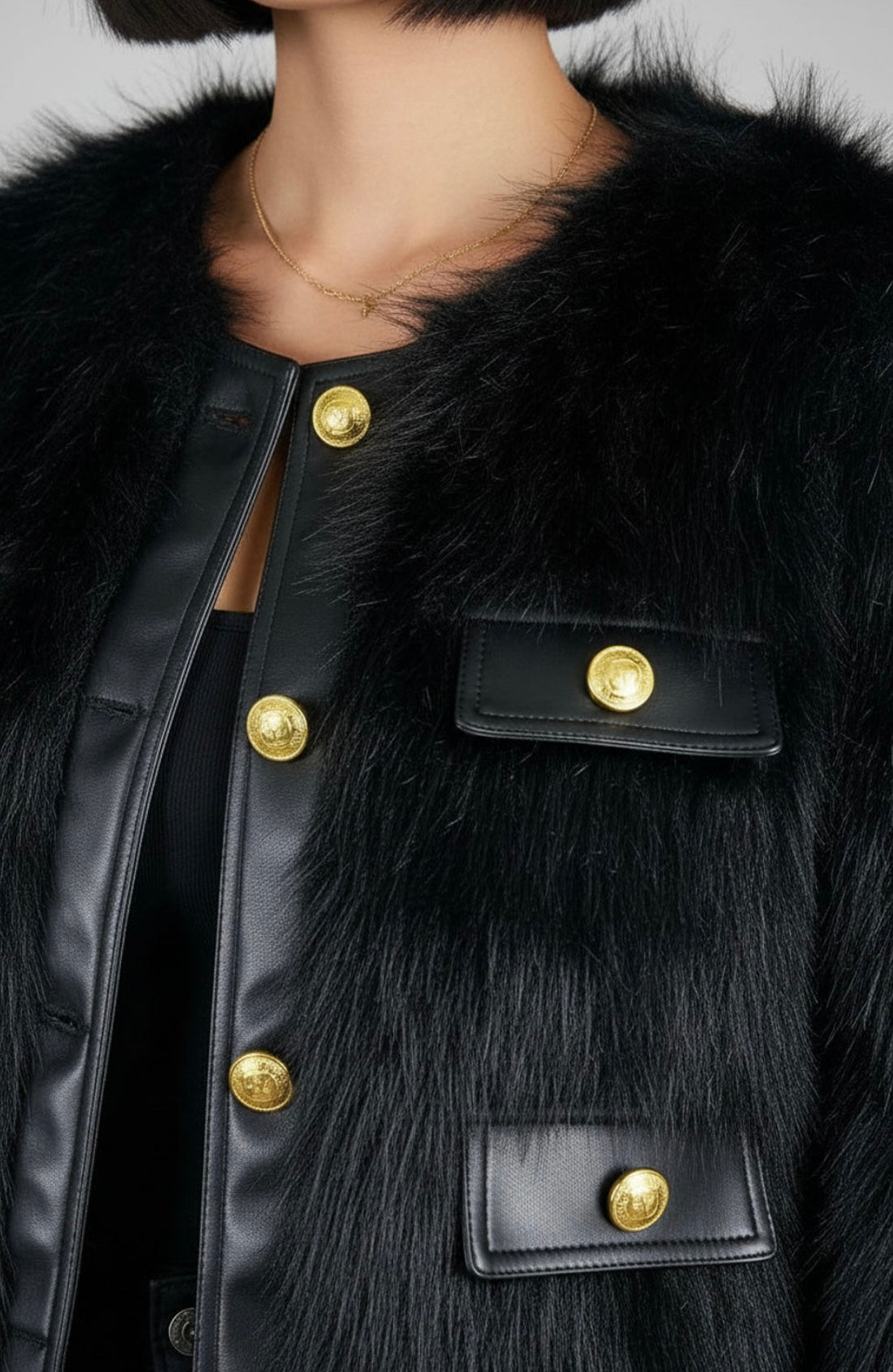 Close-up of a black fur-trimmed coat with gold buttons on a neutral background