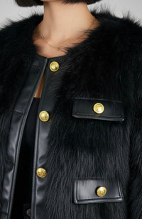 Close-up of a black fur-trimmed coat with gold buttons on a neutral background
