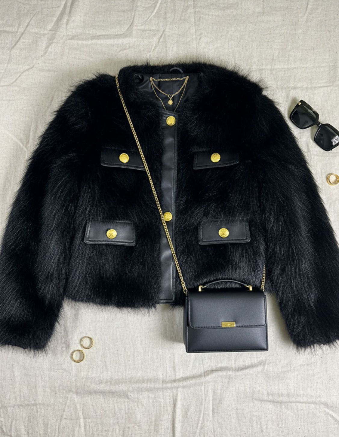 Black fur jacket with gold buttons and a matching handbag on a light gray background
