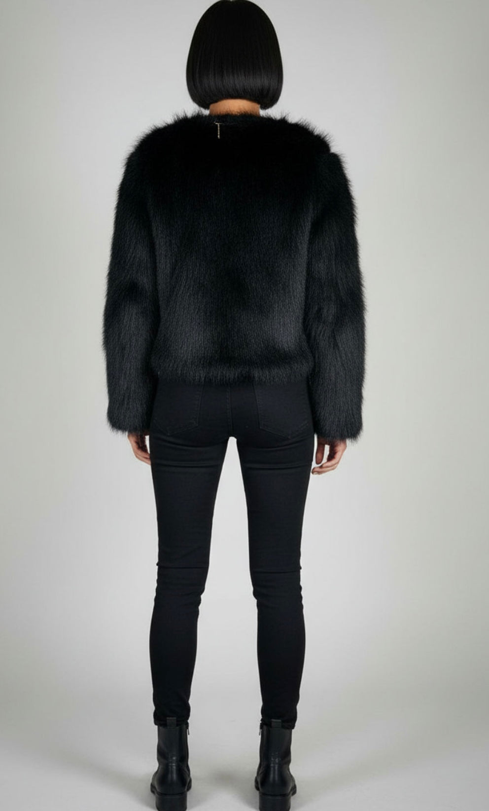 Person wearing a black fur coat and black pants on a plain background