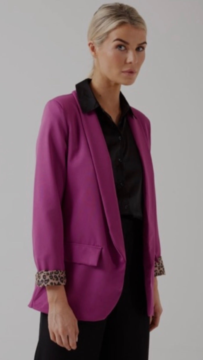Woman wearing a purple blazer with leopard print cuffs on a plain background